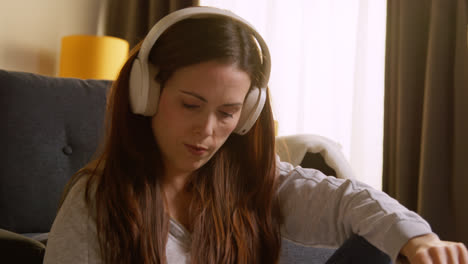 Woman-Wearing-Wireless-Headphones-Sitting-On-Floor-At-Home-Streaming-Music-From-Mobile-Phone-7